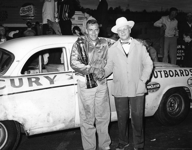 MARTINSVILLE, VA — October 28, 1956: Driver Jack Smith holds his trophy in victory lane at Martinsville Speedway, joined by car owner Carl Kiekhaefer. Smith drove Kiekhaefer’s Dodge to the win in the Old Dominion 400 NASCAR Cup race. (Photo by ISC Images & Archives via Getty Images)