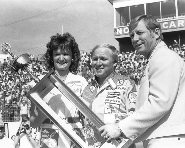 ROCKINGHAM, NC October 23, 1977: Cale Yarborough (C) is presented his trophy for being second-fast qualifier for the American 500 NASCAR Cup race by baseball legend Mickey Mantle (R) at North Carolina Motor Speedway. (Photo by ISC Images & Archives via Getty Images)