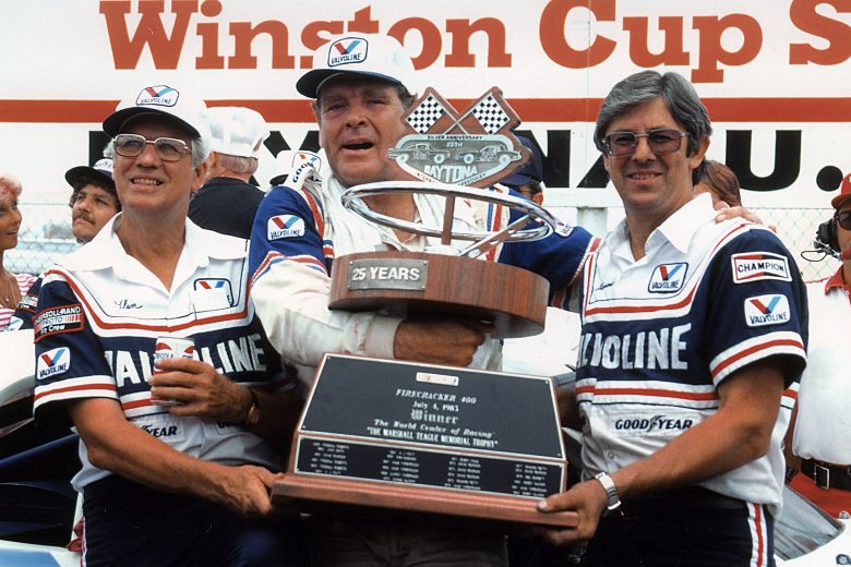 DAYTONA BEACH, FL — July 4, 1983: Buddy Baker (C) with car owners Glen (L) and Leonard Wood (R) in victory lane at Daytona International Speedway with the Marshall Teague Memorial trophy after Baker drove the Wood Brothers Valvoline Ford to victory in the Firecracker 400 NASCAR Cup race. (Photo by ISC Images & Archives via Getty Images)