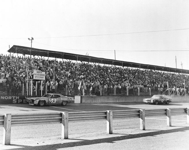 NORTH WILKESBORO, NC - OCTOBER 1, 1972: Richard Petty guides his damaged Plymouth (No. 43) under the checkered flag ahead of a smoking Bobby Allison (No. 12) to win the Wilkes 400 NASCAR Cup race at North Wilkesboro Speedway. Petty and Allison crashed into each other several times during the finial three laps of the race before Petty prevailed. (Photo by ISC Images & Archives via Getty Images)