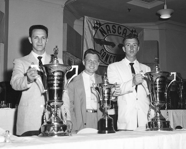 UNKNOWN — 1957: Three NASCAR Champions pose with their trophies at the NASCAR awards banquet. Ralph Earnhardt (L) was the National Sportsman champion, Fred Meeker (C) was the Midget Division titlist and Charles “Red” Farmer (R) was the National Modified champion. (Photo by ISC Images & Archives via Getty Images)