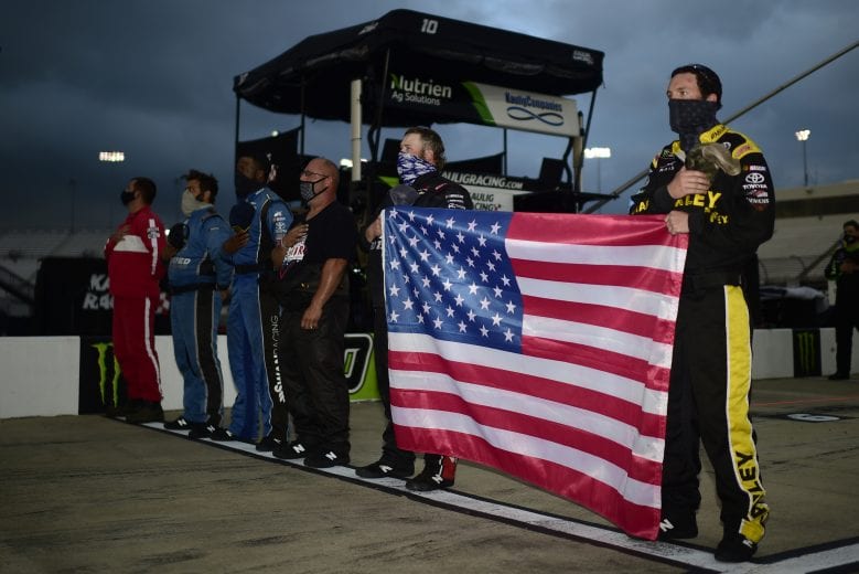RICHMOND, VIRGINIA - SEPTEMBER 11: Bayley Currey, driver of the #74 Mutt and Jeff Porkskins Inc. Chevrolet, and crew hold the American flag during pre-race ceremonies prior to the NASCAR Xfinity Series Go Bowling 250 at Richmond Raceway on September 11, 2020 in Richmond, Virginia. (Photo by Jared C. Tilton/Getty Images) | Getty Images