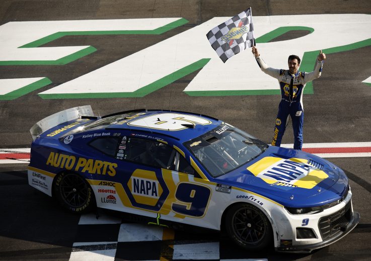 Chase Elliott stands by his car, waving the checkered flag at Atlanta