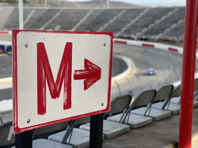 Grandstand signage points toward seating section M as Chris Buescher drives into Turn 1 at North Wilkesboro