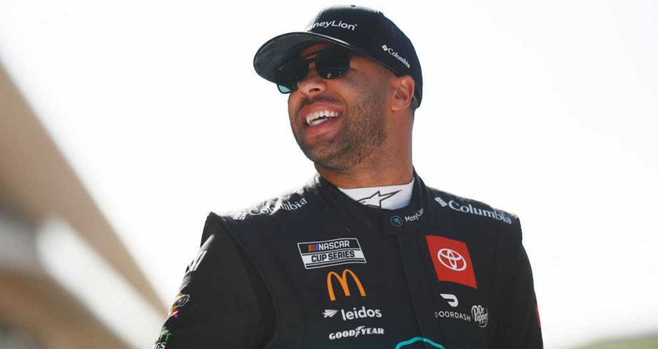Bubba Wallace smiles in the garage area at Circuit of The Americas while wearing a Money Lion fire suit.
