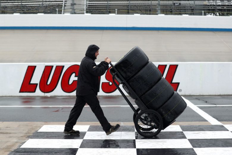 Pit crew member moves tires in rain.