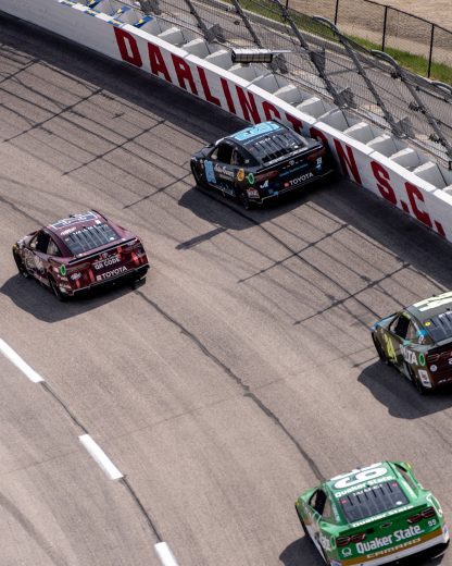 NASCAR Cup Series cars race through a turn at Darlington Raceway.