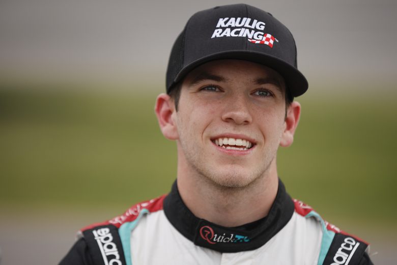 This is a close-up shot of Chandler Smith, wearing a Kaulig Racing hat, standing on pit road