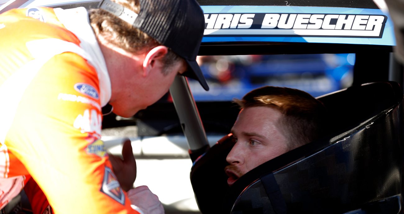 Brad Keselowski talks to Chris Buescher, seated in car, at the Clash at the Coliseum
