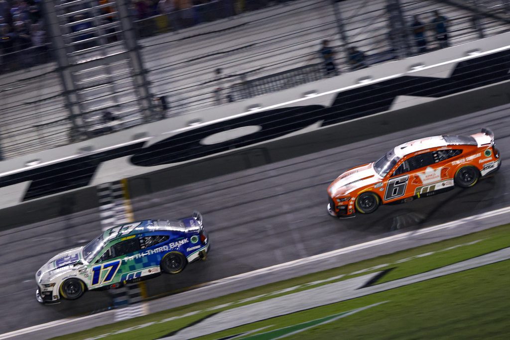 DAYTONA BEACH, FLORIDA - AUGUST 26: Chris Buescher, driver of the #17 Fifth Third Bank Ford, crosses the finish line ahead of Brad Keselowski, driver of the #6 King