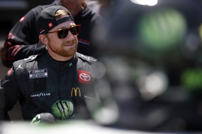 Tyler Reddick smiles on pit road while wearing backwards hat and sunglasses
