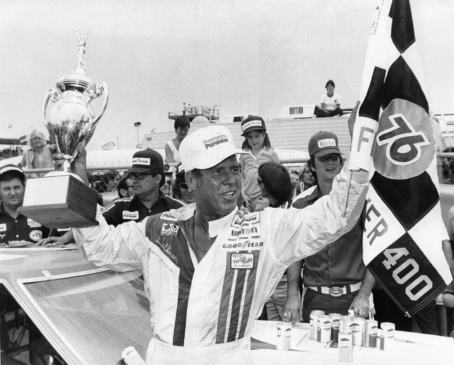 David Pearson raises trophy and checked flag.