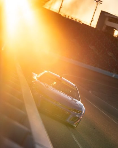 Kyle Larson drives the No. 5 Chevrolet into Turn 1 at Phoenix Raceway with the sun setting in the background during a NASCAR Cup Series test.