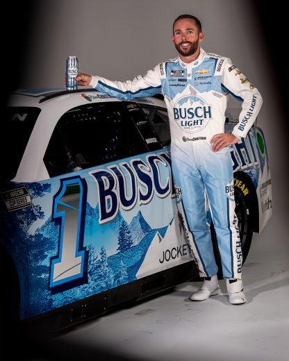 Ross Chastain standing against Busch Light Chevrolet with a Busch Light can