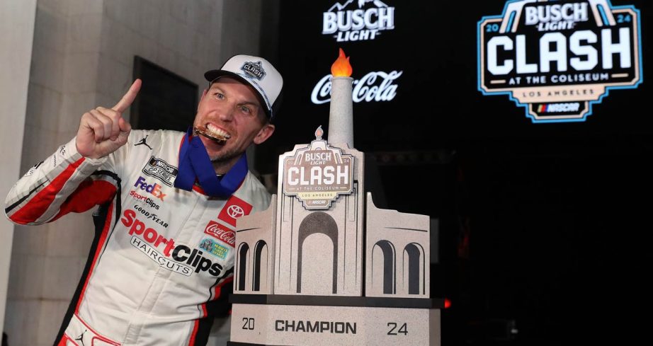 Denny Hamlin bites his first-place metal and poses with the winning trophy in Victory Lane at the Los Angeles Memorial Coliseum.