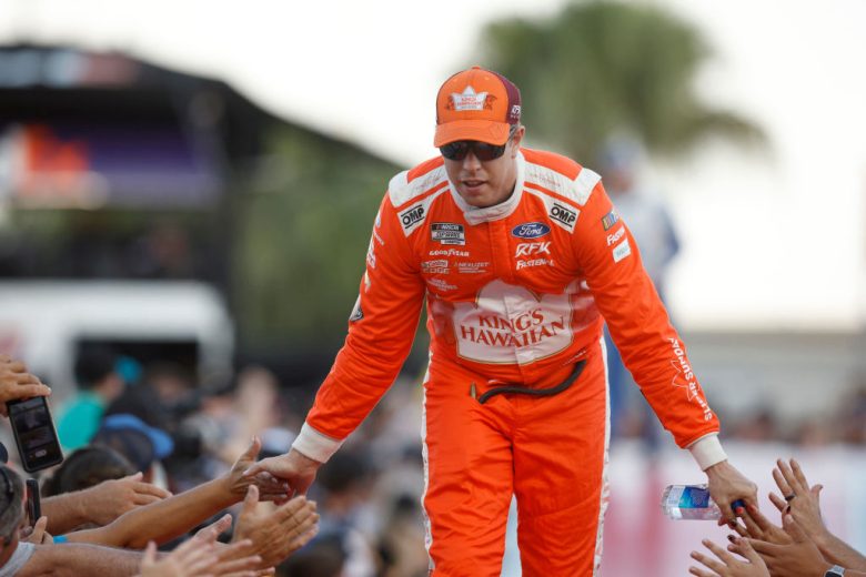 Brad Keselowski walks across the stage and claps hands with fans before a race.