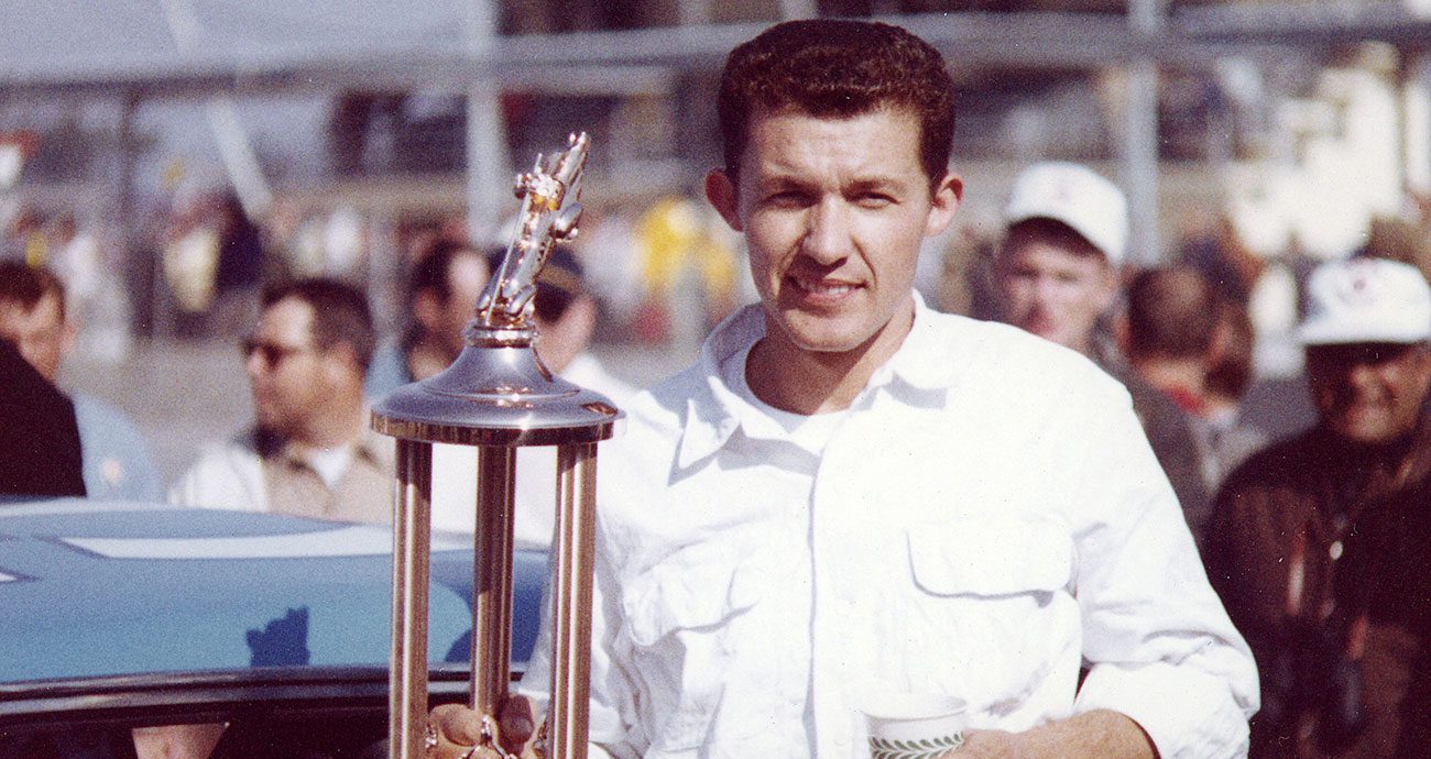 Richard Petty smiles while holding his 1964 Daytona 500 winning trophy
