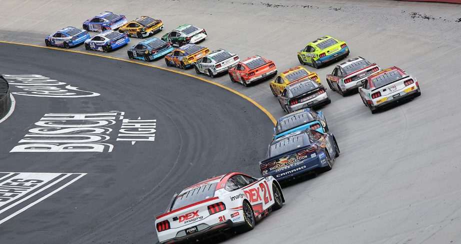 A pack of NASCAR cup cars drive around the corner.