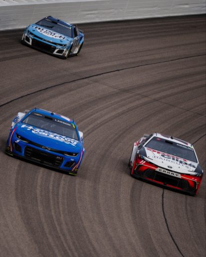 Ross Chastain (background), Kyle Larson (L) and Denny Hamlin (R) race at Kansas Speedway.