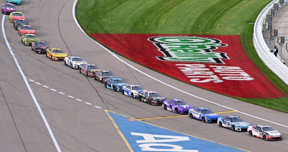 NASCAR Cup Series cars drive toward pit road at Kansas Speedway.