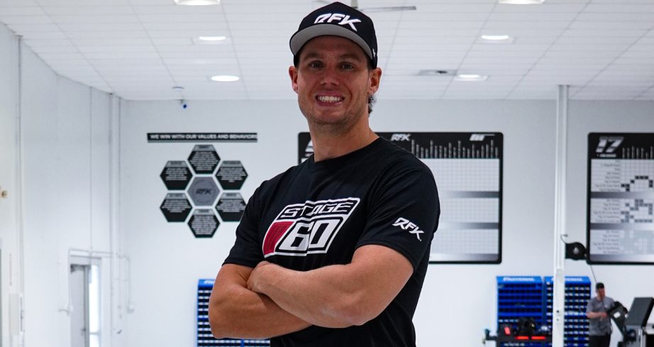 Cam Waters wears an RFK Racing hat and Stage 60 shirt in the RFK Racing shop.