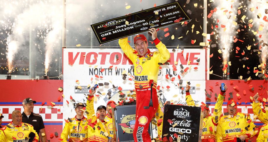 Joey Logano holds up the $1 million check for winning the All-Star Race while he and his team celebrate in Victory Lane at North Wilkesboro.