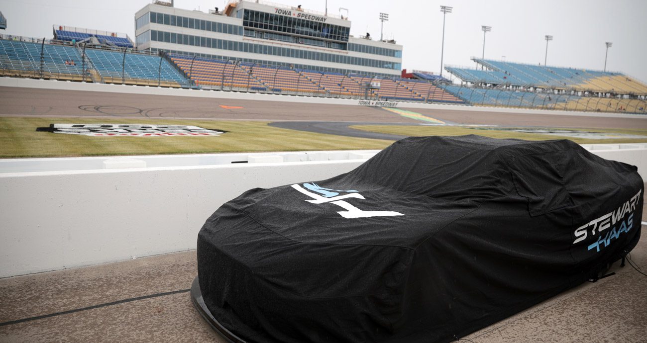 A NASCAR stock car sits under covers during rain at Iowa.
