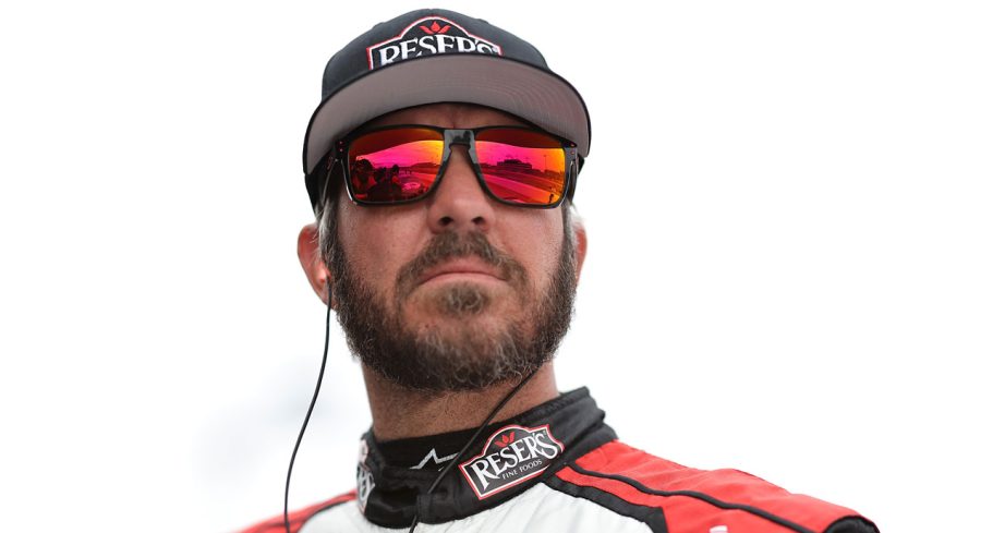 Martin Truex Jr. looks on during qualifying at Iowa Speedway while wearing a Reser's Fine Foods hat and red/orange-tinted sunglasses.