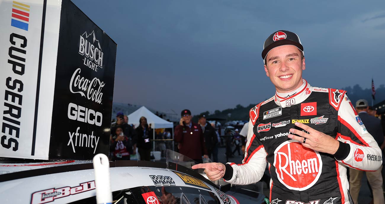 Christopher Bell poses next to his No. 20 Joe Gibbs Racing Toyota and points to the winner sticker placed on the machine following his NASCAR Cup Series win at New Hampshire Motor Speedway.