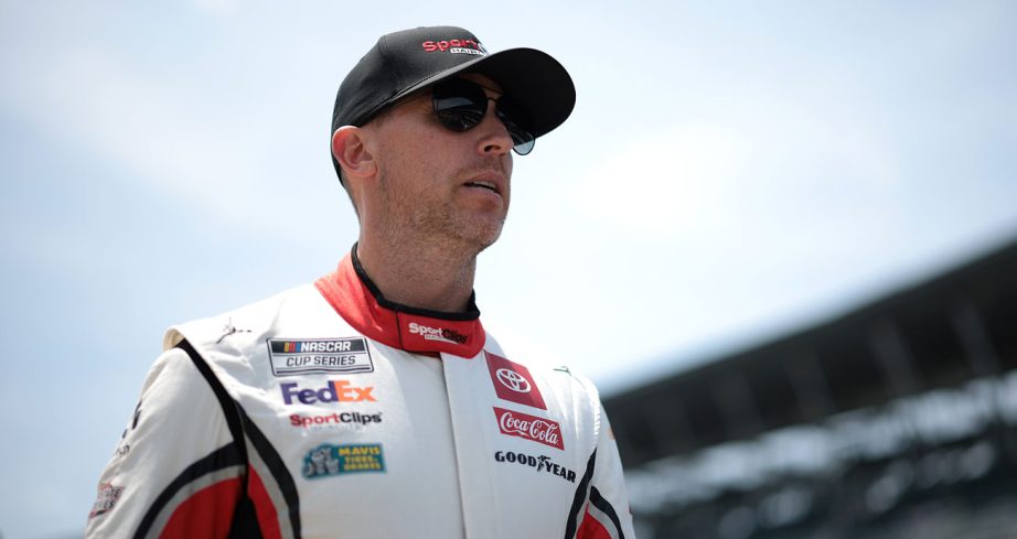 Denny Hamlin walks the grid at Indianapolis Motor Speedway while wearing an red and white Sport Clips Haircuts fire suit.