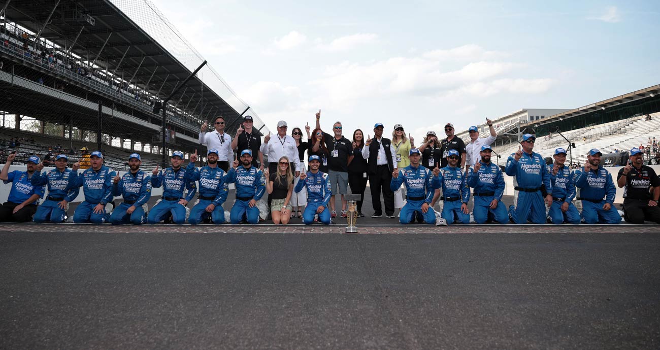 Kyle Larson and his No. 5 Hendrick Motorsports pit crew pose for a photo on the start/finish line at Indianapolis Motor Speedway.