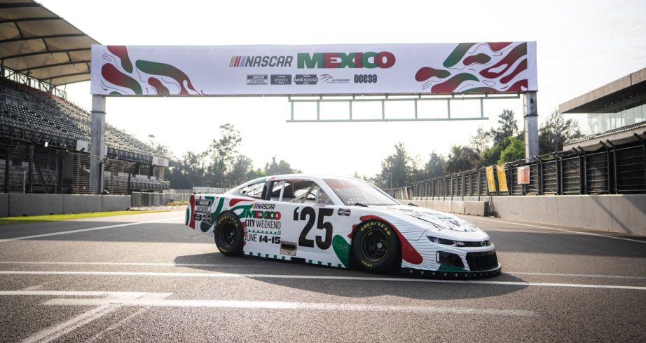 A stock car sits in front of a NASCAR Mexico banner, at the track