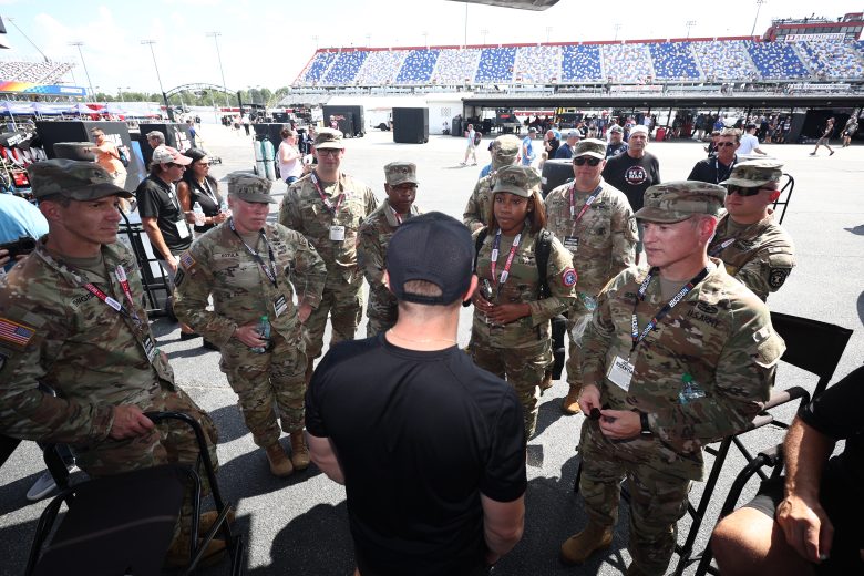 A background shot of Ricky Stenhouse Jr. speaking with U.S. military service members.