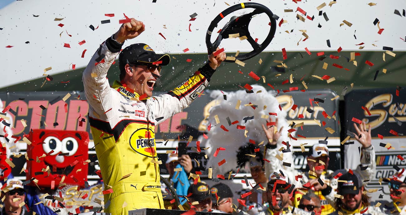 Joey Logano celebrates in Victory Lane at Las Vegas Motor Speedway while holding his steering wheel in his left hand.