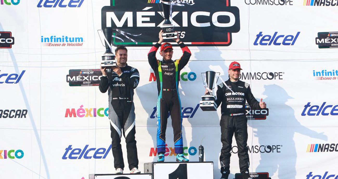 Abraham Calderon stands on podium top step holding trophy. 