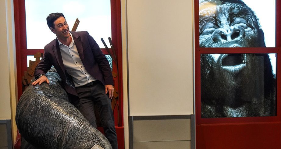 Joey Logano poses for photo while being held by replica gorilla.