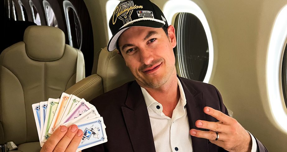 Joey Logano holds up cards in one hand and three finigers with the others while on a plane.
