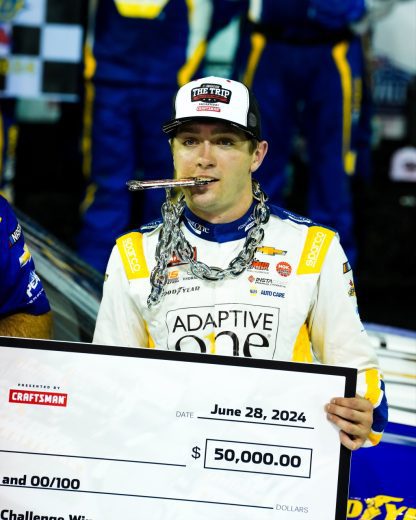 Christian Eckes holds the Triple Truck Challenge check while biting down on a chain following his NASCAR Craftsman Truck Series win at Nashville Superspeedway.