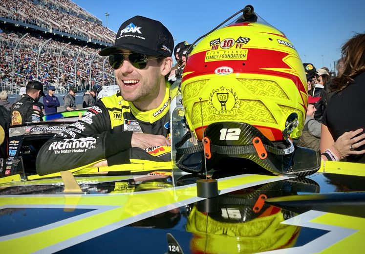 Ryan Blaney smiles with his No. 12 Team Penske Ford driver helmet perched in the foreground at Daytona International Speedway.