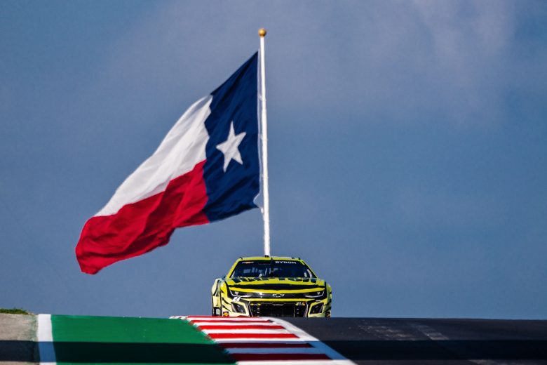 William Byron's No. 24 Chevrolet races at Circuit of The Americas as the Texas flag waves in the background.