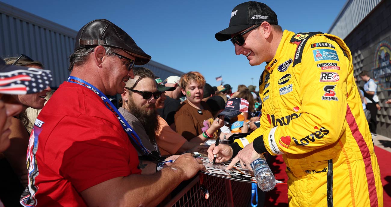 Michael McDowell (R) signs autographs for fans before a NASCAR Cup Series race.