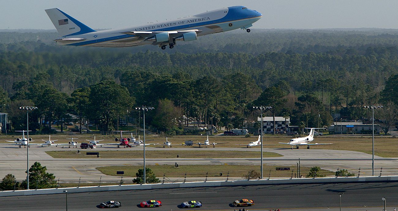 View of Air Force One flying over Daytona International Speedway in 2004 with cars on track.