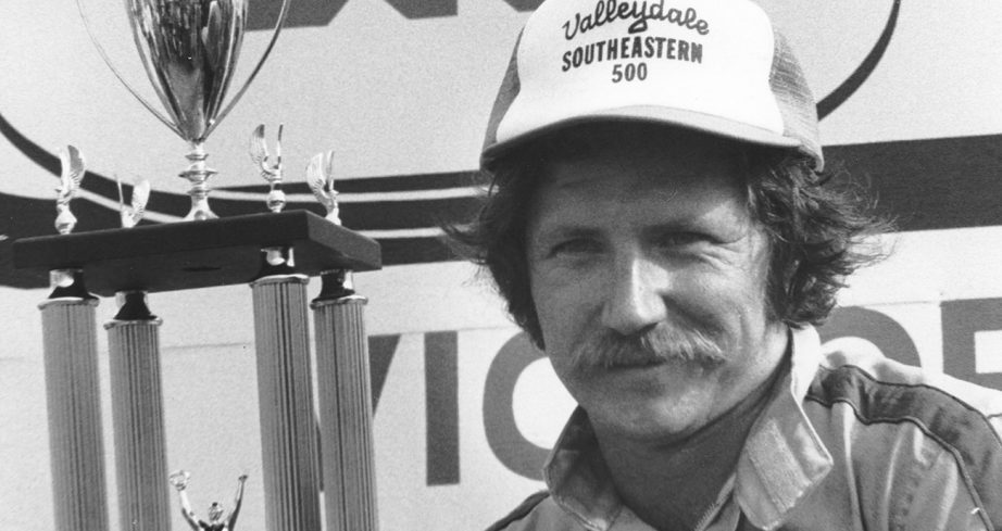 Dale Earnhardt smiles as he sits next to trophy.
