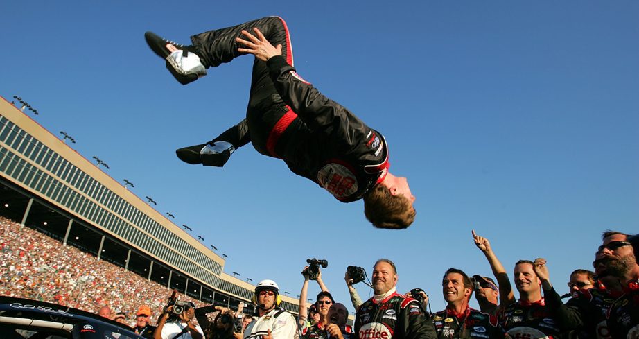 Carl Edwards does a backflip off car with his crew standing Victory Lane at Atlanta Motor Speedway.