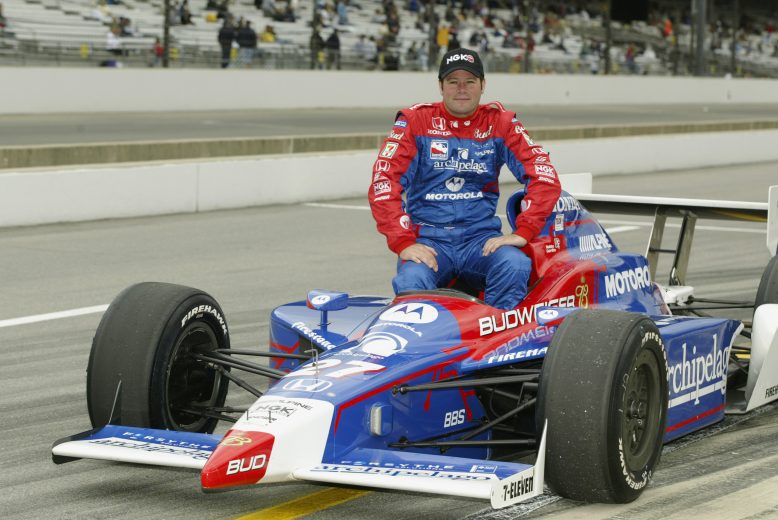 Robby Gordon smiles as he sits on top of his IndyCar.