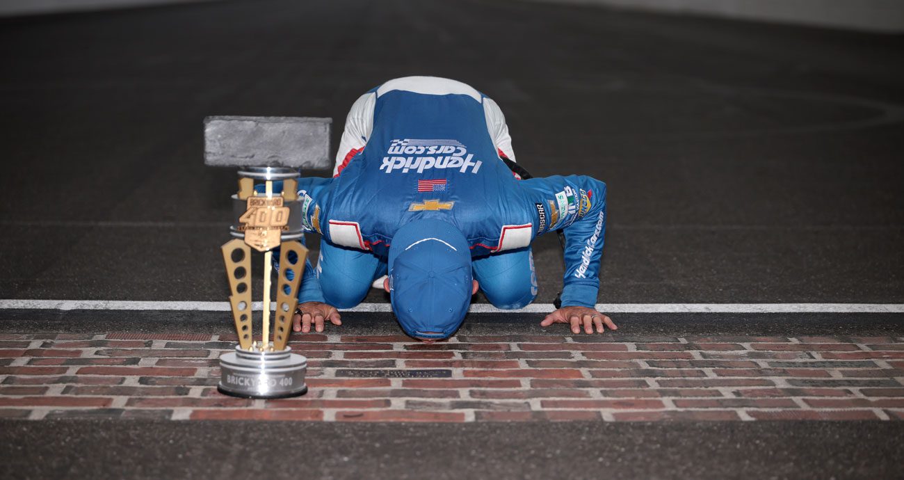 Kyle Larson kisses the bricks at Indianapolis Motor Speedway with the winner trophy in the foreground following his NASCAR Cup Series win at Indianapolis Motor Speedway.