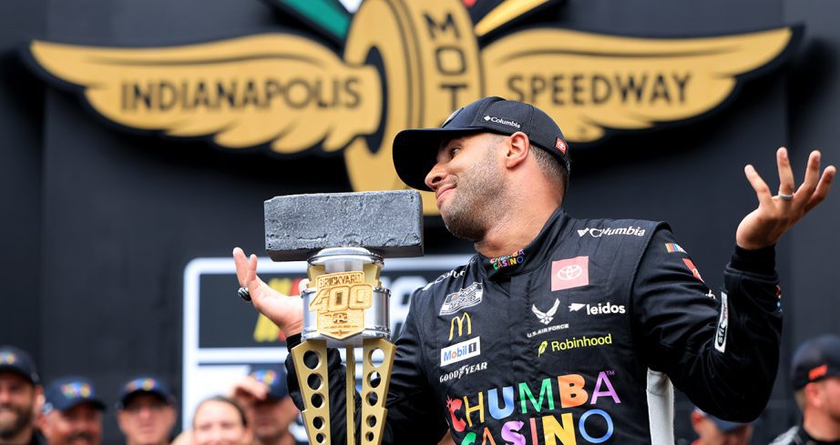 Bubba Wallace shrugs his shoulders while standing next to Brickyard 400 trophy.