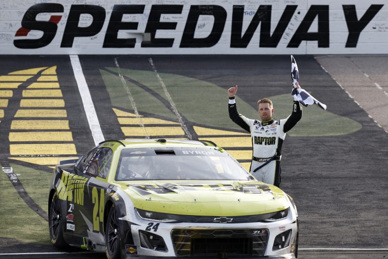 William Byron stands next to his No. 24 Hendrick Motorsports Chevrolet while holding the checkered flag and celebrates following his NASCAR Cup Series win at Iowa Speedway.