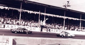 Ned Jarrett crosses under the checkered flag to win the 1965 Southern 500 at Darlington Raceway by a record 19-plus miles (14 laps). Behind him is the runner-up No. 86 driven by Buddy Baker in relief of his father, Buck.