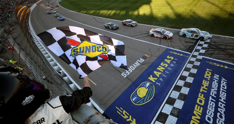 Chase Elliott's No. 9 Hendrick Motorsports Chevrolet crosses the start/finish line at Kansas Speedway as the checkered flag waves in the foreground.